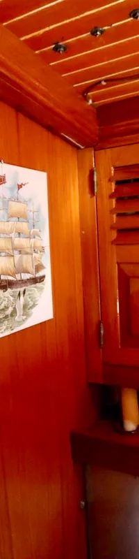 De foto toont een interieur met houten lambrisering, een kapstok, een tegel met een zeilschip en een houten kast met…