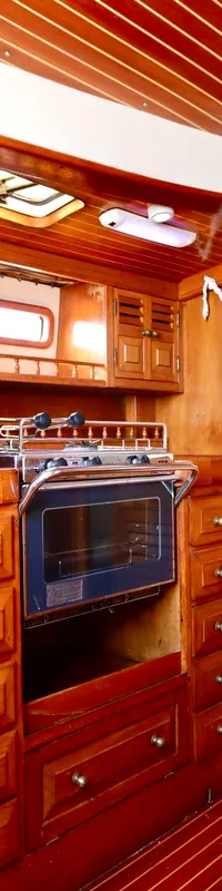 Een houten bootinterieur met een kombuis, inclusief een fornuis met oven, een gootsteen en diverse kasten.