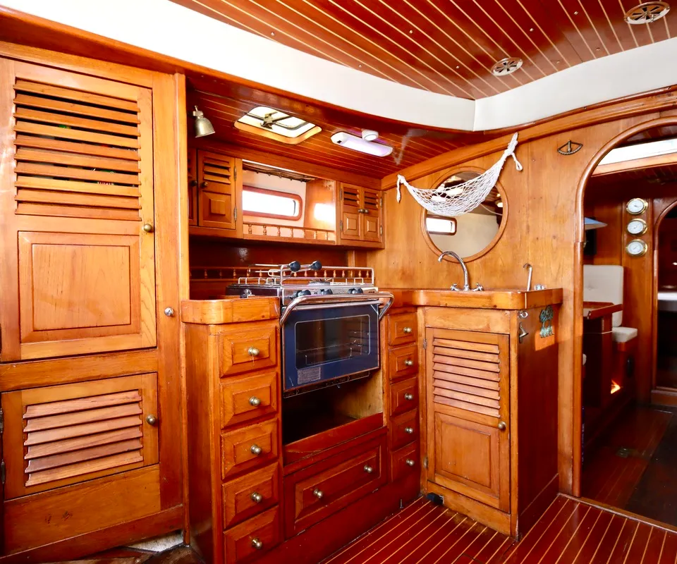 Een houten bootinterieur met een kombuis, inclusief een fornuis met oven, een gootsteen en diverse kasten.
