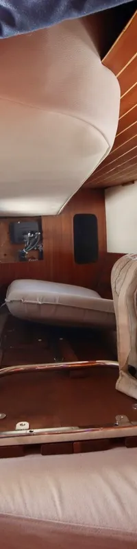 De foto toont een interieur van een boot met houten afwerking, kussens en een raam dat uitzicht biedt op een andere boot.