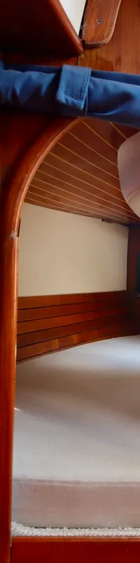 Een kajuit met houten lamellenkast, een bed met wit matras en een raam met uitzicht op het dek. — RJ 140