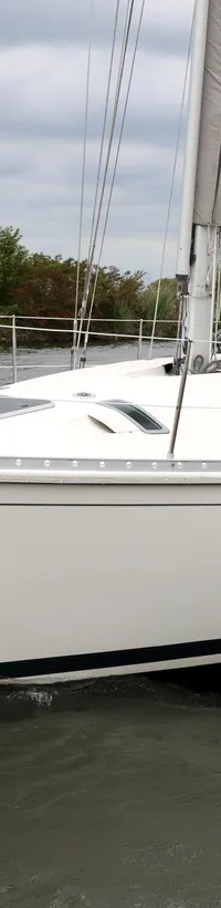 Een witte zeilboot met de naam "BENETEAU" op de boeg vaart op water met een gebouw op de achtergrond. — Beneteau First 41S5