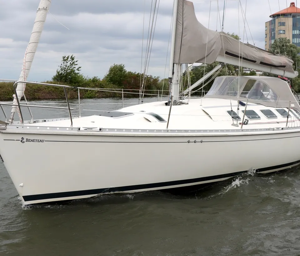 Een witte zeilboot met de naam "BENETEAU" op de boeg vaart op water met een gebouw op de achtergrond. — Beneteau First 41S5
