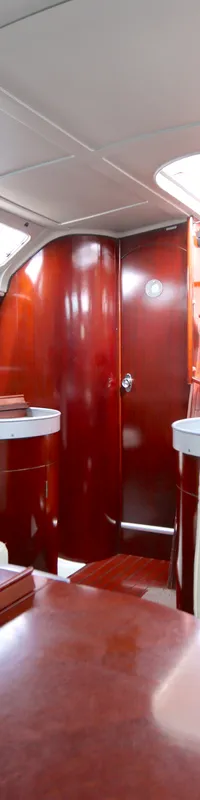 De foto toont het interieur van een boot met houten wanden, witte banken, een tafel en een kombuis met spoelbakken.