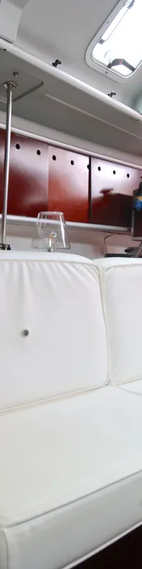 De foto toont een interieur van een boot met witte banken, houten kasten en een aantal ramen in het plafond.