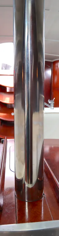 De foto toont het interieur van een boot met een houten vloer, witte banken, een ronde houten tafel en een zilverkleurige…