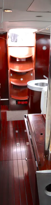 De foto toont het interieur van een boot met witte banken, een houten vloer en een tafel met een metalen paal.
