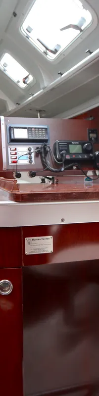 De foto toont het interieur van een boot met een houten afwerking, een navigatiehoek en een zithoek met witte kussens.