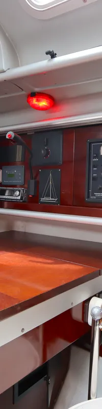 De foto toont een interieur van een boot met een houten tafel, diverse navigatie- en communicatieapparatuur, en een…