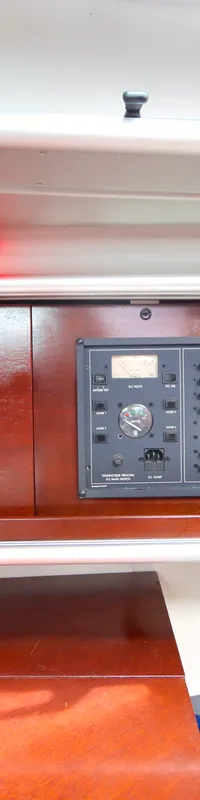 Een interieur van een boot met een houten dashboard, diverse meters, schakelaars, een radio en een rood licht.