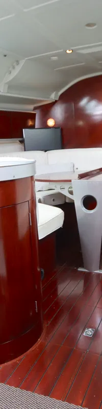 De foto toont het interieur van een boot met een houten vloer, donkerhouten meubels, een kombuis en een navigatiehoek.