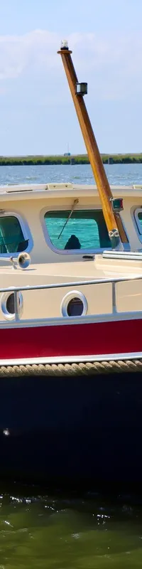 Een man staat achter het stuur van een donkerblauwe boot met rode en crèmekleurige accenten, varend op water.