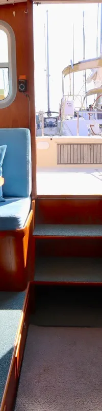 De kajuit toont een houten interieur met ramen, een tafel met blauwe kussens, een kombuis met twee spoelbakken en een…