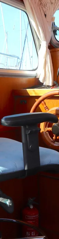 Een houten interieur van een boot met een stuurwiel, een blauwe stoel, een instrumentenpaneel en ramen met gordijnen.