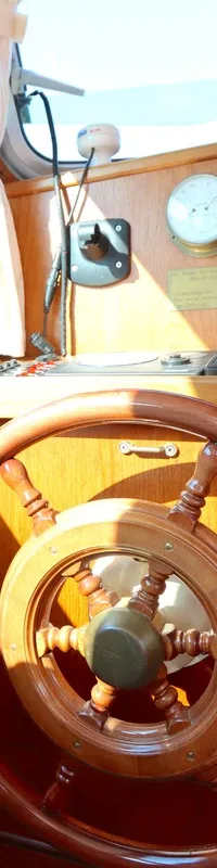 Een houten stuurwiel en dashboard met meters en bedieningselementen zijn zichtbaar in de stuurhut van een boot.
