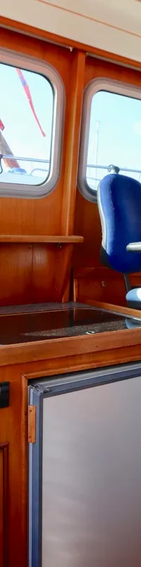 De kajuit toont een houten interieur met ramen, een stuurstand met houten stuurwiel en blauwe stoel, en een kombuis met…