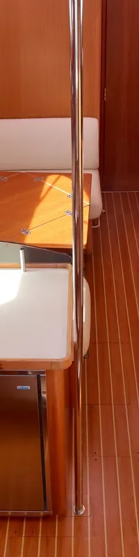 De kajuit toont een houten interieur met een kombuis, twee tafels, witte zitbanken en een gestreepte houten vloer.