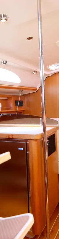 De kajuit toont een houten interieur met een kombuis, zitbanken met lichte kussens, tafels, een koelkast en patrijspoorten.