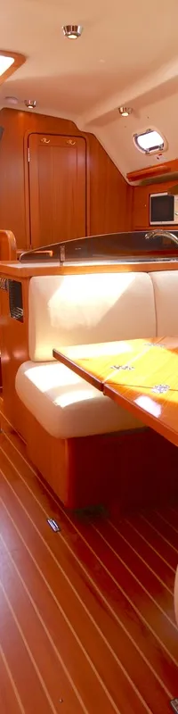 De kajuit toont een houten interieur met lichte kussens, een houten tafel, een kombuis en een trap naar het dek.