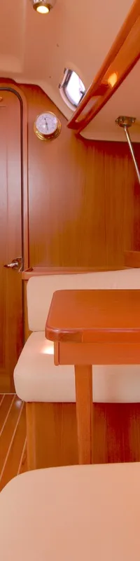De kajuit toont een houten interieur met lichte banken, een tafel, een deur, een patrijspoort en een gestreepte vloer.