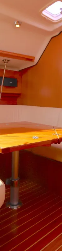 De foto toont een bootinterieur met een U-vormige bank met lichte bekleding, een houten tafel, houten wanden en vloer, en…