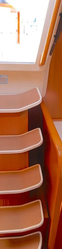 De foto toont een houten kajuitinterieur met een trap naar boven, omringd door deuren en kasten, en een raam bovenaan.