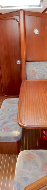 De kajuit toont een houten interieur met een kombuis, zithoek met tafel en stoffen kussens, en een houten vloer.