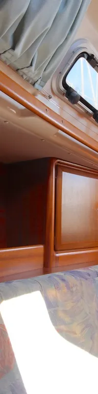 De kajuit toont een houten interieur met een zithoek met patroon kussens, ramen, kastjes en een plafondlamp.