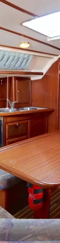 De foto toont een houten interieur van een boot met een kombuis, zithoek met kussens, tafel en een brandblusser.