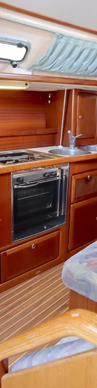 De foto toont een houten bootinterieur met een kombuis, een eettafel met banken en een brandblusser op de vloer.
