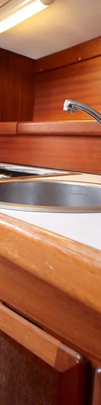De foto toont een houten scheepsinterieur met een witte aanrecht, twee roestvrijstalen spoelbakken, een kraan en een oven.