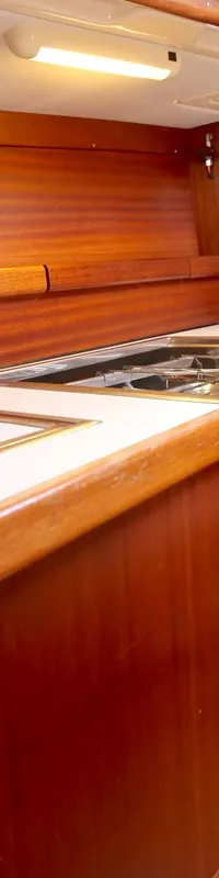 De foto toont een scheepskeuken met houten kasten, een aanrecht, een fornuis met oven en een dubbele spoelbak.