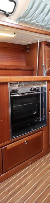 Een houten scheepsinterieur met kombuis, fornuis met oven, spoelbak, kasten, een bankje en een tafel.