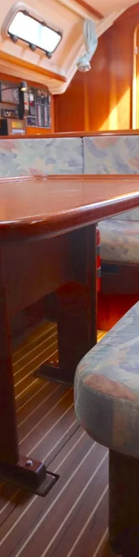 Een houten kajuit met een tafel en banken met lichtblauwe, roze en groene kussens, en een houten vloer. — Bavaria 35 Holiday
