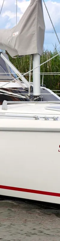 Een witte zeilboot met de naam "SAMA" en een rode streep op de romp vaart op het water, met een persoon aan boord. — Etap 30i