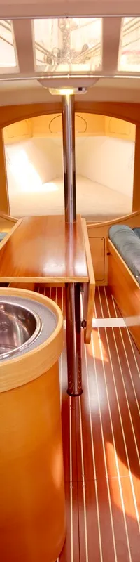 Het interieur van de boot toont een kombuis met gootsteen en fornuis, een zithoek met blauwe kussens en een houten tafel.