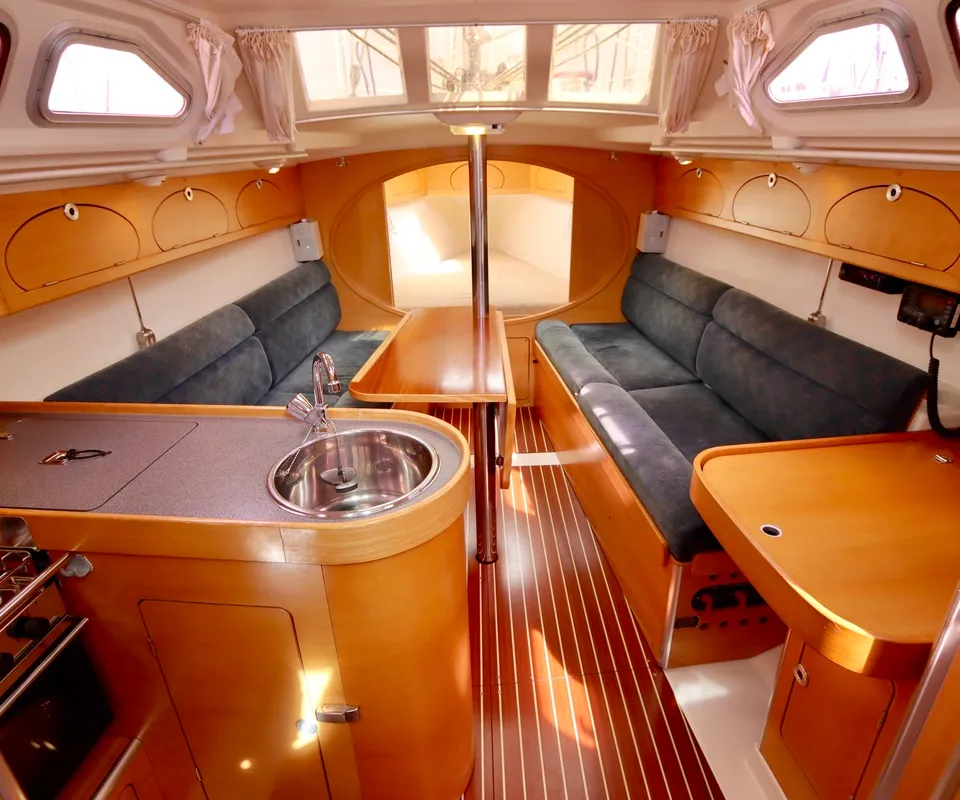 Het interieur van de boot toont een kombuis met gootsteen en fornuis, een zithoek met blauwe kussens en een houten tafel.