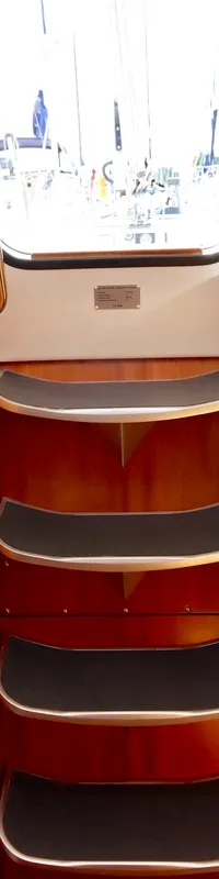 De foto toont het interieur van een boot met een centrale trap, een toiletruimte links en een slaapcabine met kombuis rechts.
