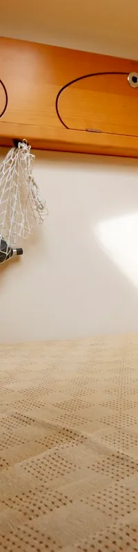 Een kajuit met een bed met lichtbruine sprei, daarboven houten kasten en een wit net met een zwart voorwerp. — Etap 30i
