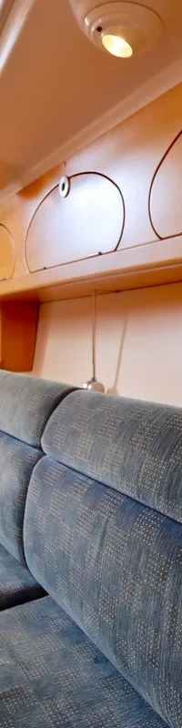 De kajuit toont een blauwe gestoffeerde bank, houten kasten met ronde deurtjes, een tafel en een kombuis met kraan.