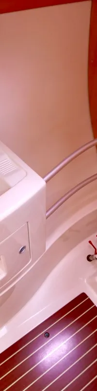 Een boottoiletruimte met een wasbak, kraan, toilet, houten kasten en een houten vloerrooster is zichtbaar.