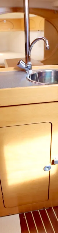 Een bootinterieur met een kombuisblok met spoelbak en kooktoestel, omringd door houten kasten en blauwe zitbanken, en een…