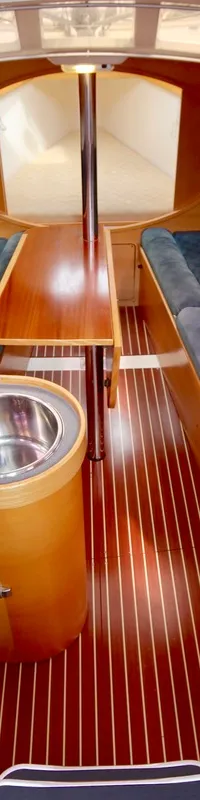 De kajuit van een boot is zichtbaar, met een kombuis aan bakboord, twee banken met blauwe kussens en een houten tafel.