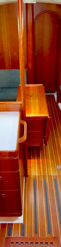 De foto toont een houten bootinterieur met een kombuis, twee banken met groene kussens en een houten vloer.
