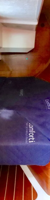 Een bootkajuit met een blauw matras, houten betimmering, kasten en een klein raam is zichtbaar.