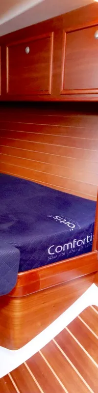 Een kajuit met een donkerblauw matras, houten wanden, houten vloer met witte strepen en houten kasten is zichtbaar.