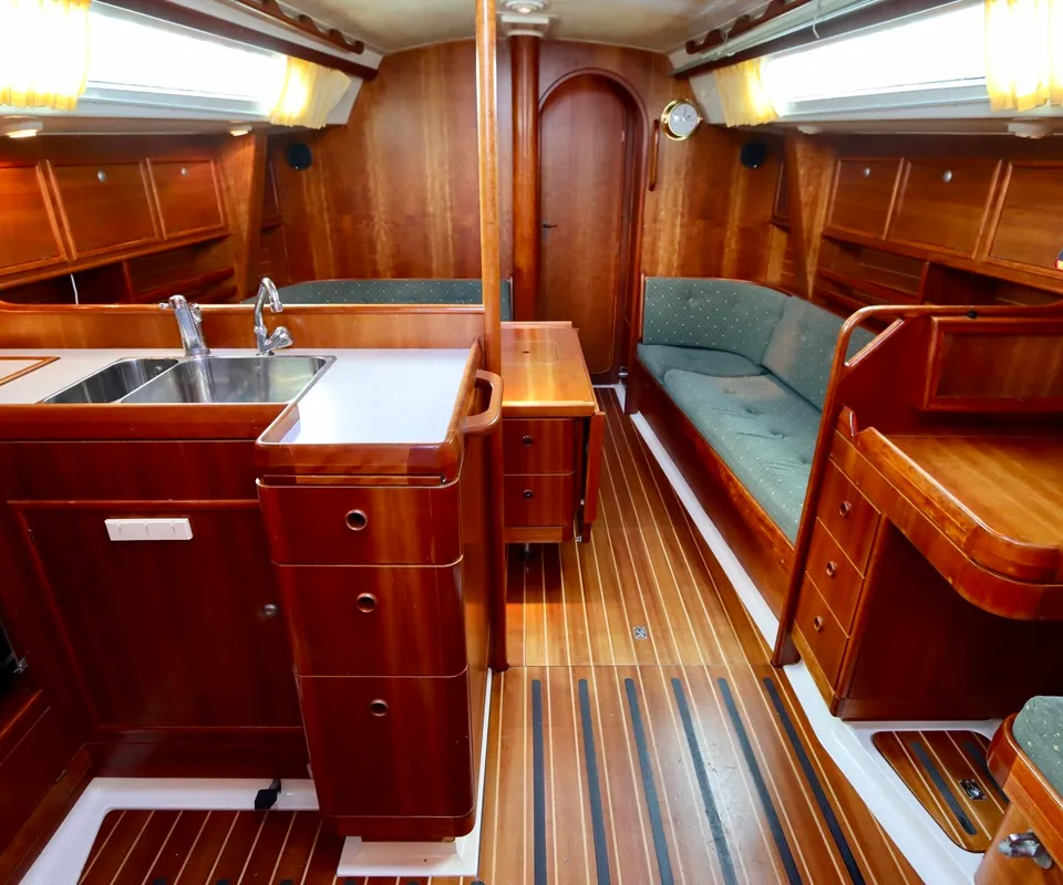 De kajuit van een boot is zichtbaar, met een houten interieur, een kombuis met dubbele spoelbak en een zithoek met groene…