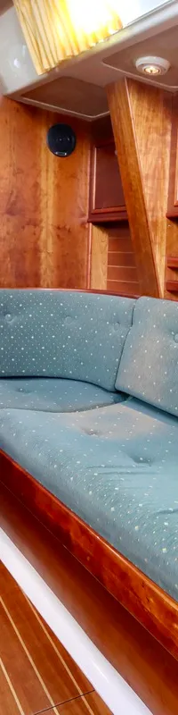 De foto toont een houten bootinterieur met een tafel, groene bankkussens, een deur, kasten en een klok aan de wand.