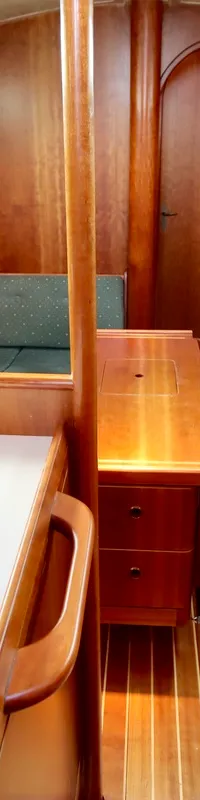 De foto toont een houten kajuitinterieur met een kombuis met dubbele spoelbak en twee groene gestoffeerde banken.