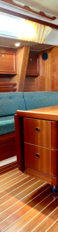 Een houten interieur met gestreepte vloer, groene banken, een inklapbare tafel met lades, een kombuis en een deur.